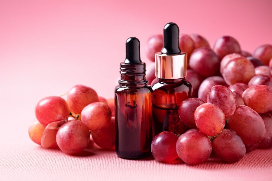 Two bottles of serum with grapes next to them.